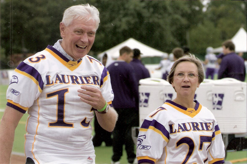A man and woman walking together wearing white, purple and yellow jerseys.